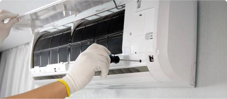 Gloved hands servicing an indoor air conditioner with its filter cover open